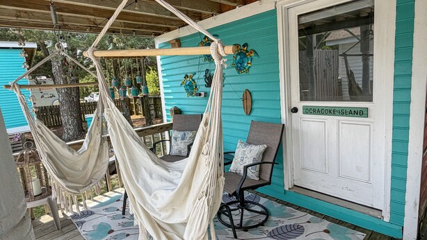 A hammock chair on a porch with a teal wall and a door labeled 'OCRACOKE ISLAND'.