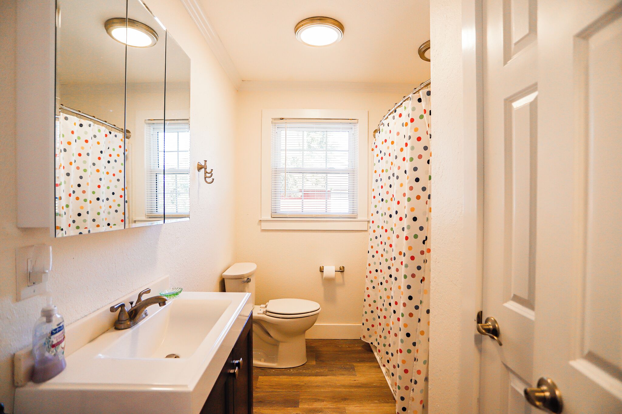 Une salle de bain avec un lavabo blanc, des toilettes et un rideau de douche à pois.