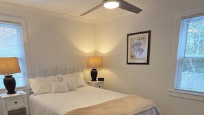 Un dormitorio con cama, mesitas de noche, ventilador de techo y ventana con persianas.