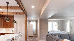 A modern kitchen with wooden beams, white cabinets, and pendant lighting. A dining area with a white table and chairs is visible through an open door. - DC51: Walter's Watch - Brand New Construction (Ocracoke)