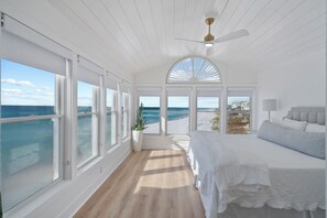 A bedroom with a large bed, a potted plant, and a view of the ocean.