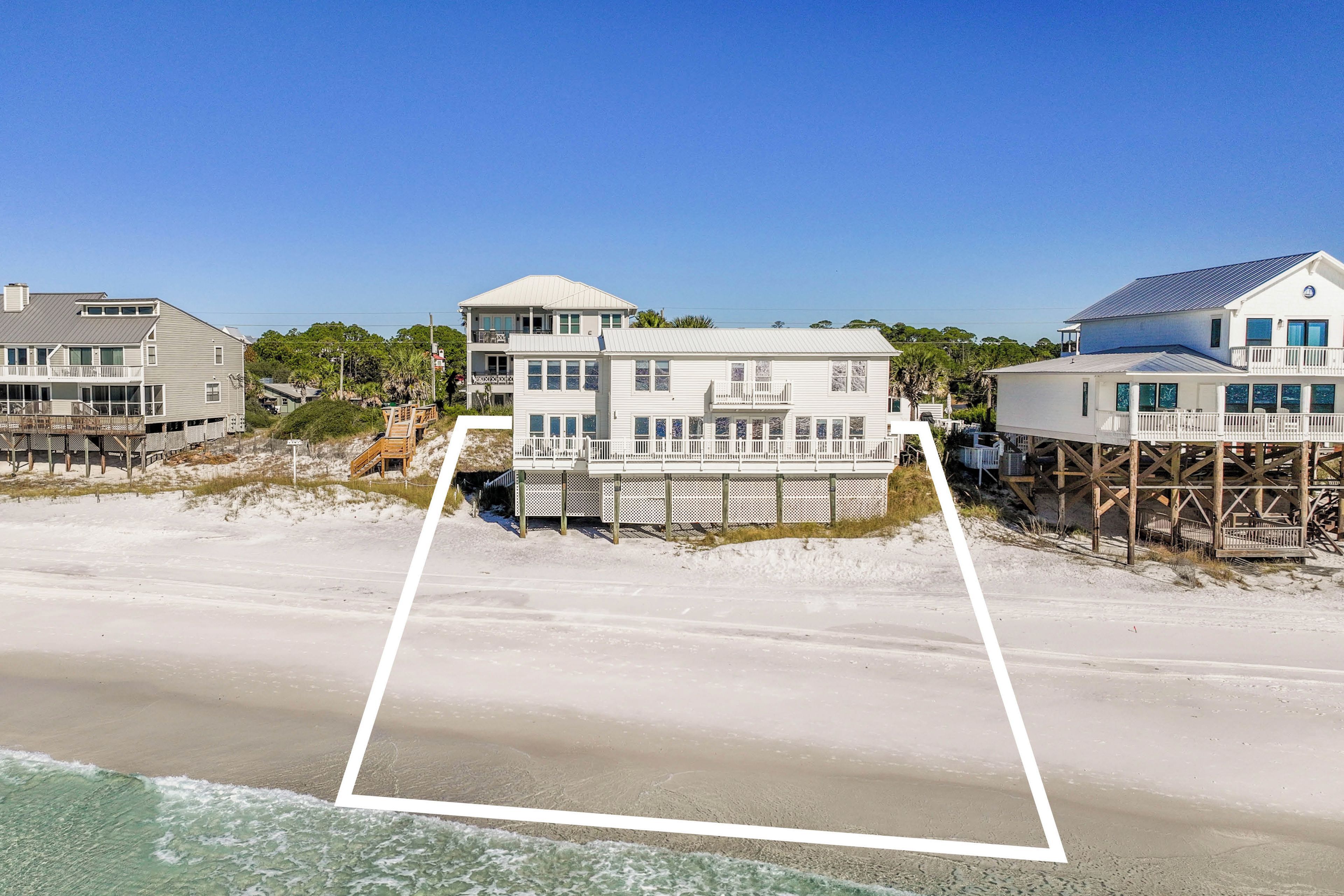 A beachfront property with multiple buildings, including a large house with a balcony and a smaller structure on stilts.