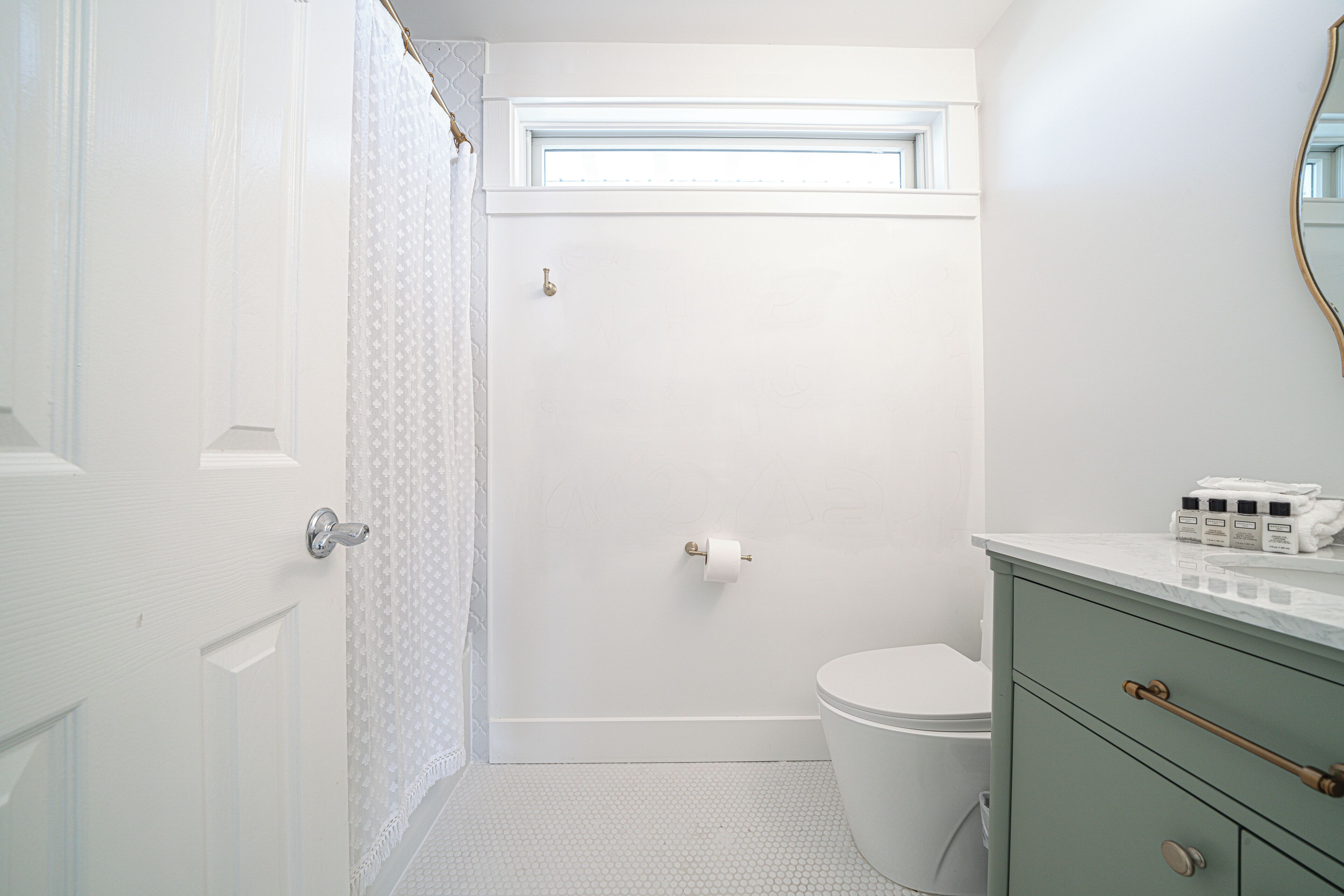 A bathroom with a toilet, a shower, a vanity with a mirror, and a window above the toilet.
