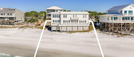 A beachfront property with multiple buildings, including a large house with a balcony and a smaller structure on stilts.