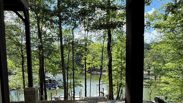 A patio with a view of a lake, surrounded by trees and a wooden deck.