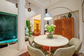 A dining area with a round table, chairs, a vase of flowers, a floor lamp, and a decorative cabinet.