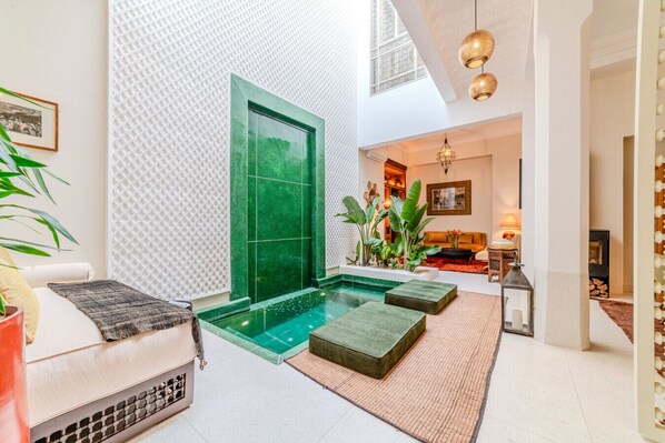 A modern interior with a green-tiled wall, a small indoor pool, and a seating area with cushions and a plant.