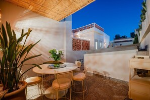 A terrace with a round table and chairs, potted plants, and a view of a modern building.