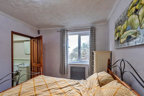 A bedroom with a bed, a window with curtains, a radiator, and a painting on the wall.
