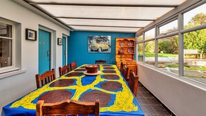 Een eetgedeelte met een lange tafel, overdekt met een kleurrijke tafelkleed, houten stoelen en een blauwe deur.