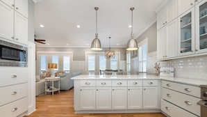 Una cocina moderna con armarios blancos, una isla central, iluminación colgante y un microondas.