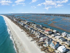 An aerial view of a coastal residential area with houses along the beach and a marshy area in the background.