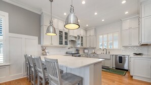 Una cocina con armarios blancos, una isla central con taburetes de bar, iluminación colgante y lavavajillas.
