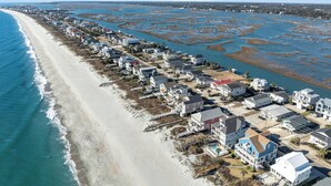 Vista aérea de una zona residencial costera con casas a lo largo de la playa y un área pantanosa al fondo.