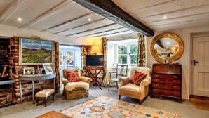 A cozy living room with exposed wooden beams, a fireplace, a television, and a large window with curtains. - Whitley (Molland)