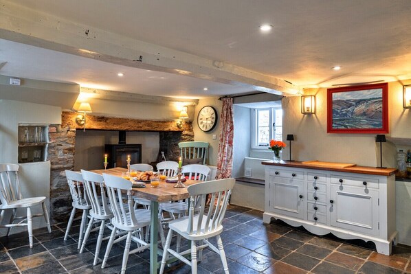 A cozy dining area with a stone fireplace, white wooden chairs, and a tiled floor. - Whitley (Molland)