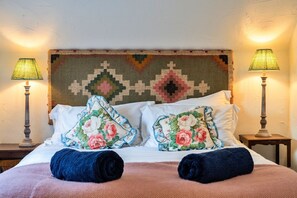 A bed with floral pillows, two bedside lamps, and a textured wall hanging. - Whitley (Molland)
