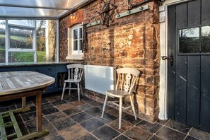 A rustic stone building with a wooden table and two chairs, a window, and a door. - Whitley (Molland)