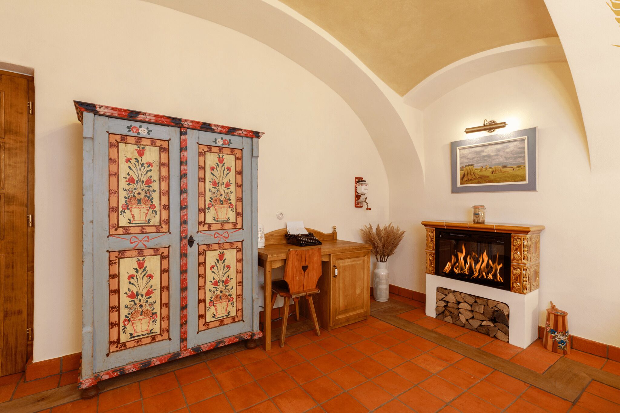 A room with a wooden desk, a chair, a fireplace, and a decorative cabinet with floral patterns.