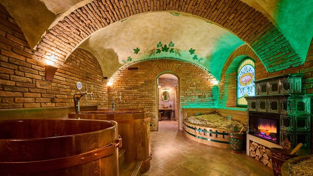 Un edificio histórico con arcos de ladrillo, grandes tinas de elaboración de cerveza de cobre y una chimenea iluminada con luz verde.
