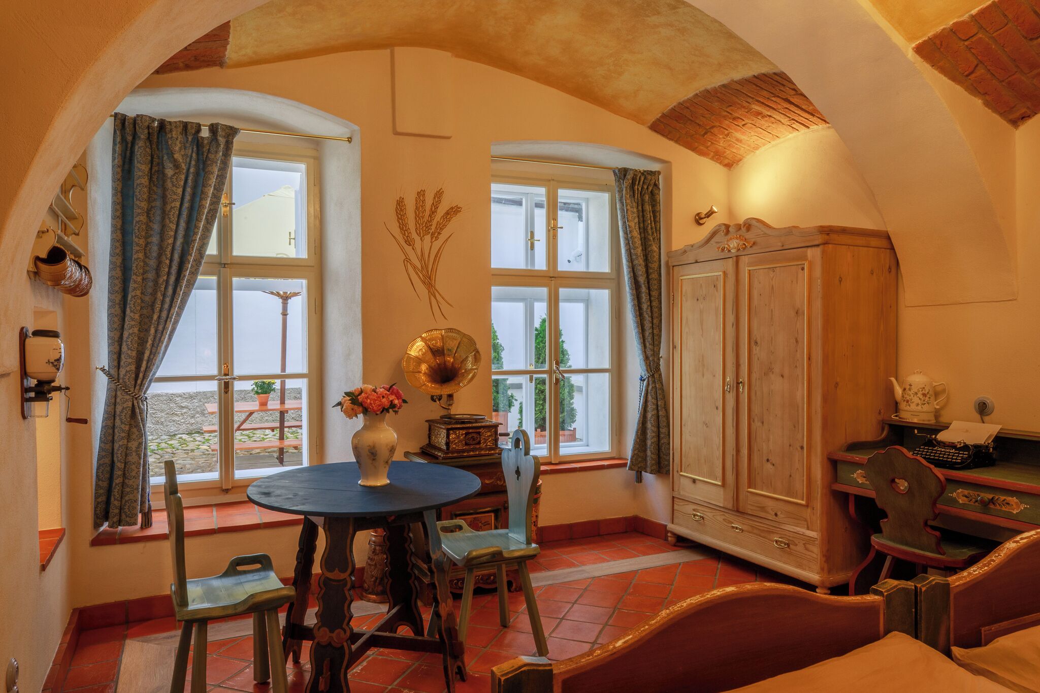 A room with a round table, chairs, a wooden cabinet, and a window with curtains.