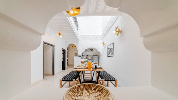 A dining area with a high ceiling and skylight, a round woven table, and a bench. - Riad Ines 10min from the medina - Swimming pool - Breakfast (Marrakech)
