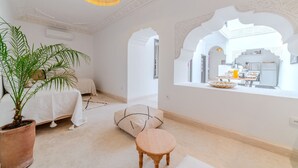 A modern, minimalist room with a large potted plant, a small wooden stool, and a view of a kitchen through an arched doorway. - Riad Ines 10min from the medina - Swimming pool - Breakfast (Marrakech)