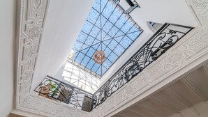 A high-ceilinged room with intricate white wall and ceiling designs, a skylight with a decorative glass ceiling, and a balcony with ornate metal railings. - Riad Ines 10min from the medina - Swimming pool - Breakfast (Marrakech)