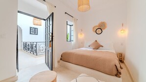 A bedroom with a bed, a small stool, a hanging light fixture, and a view of an outdoor balcony. - Riad Ines 10min from the medina - Swimming pool - Breakfast (Marrakech)