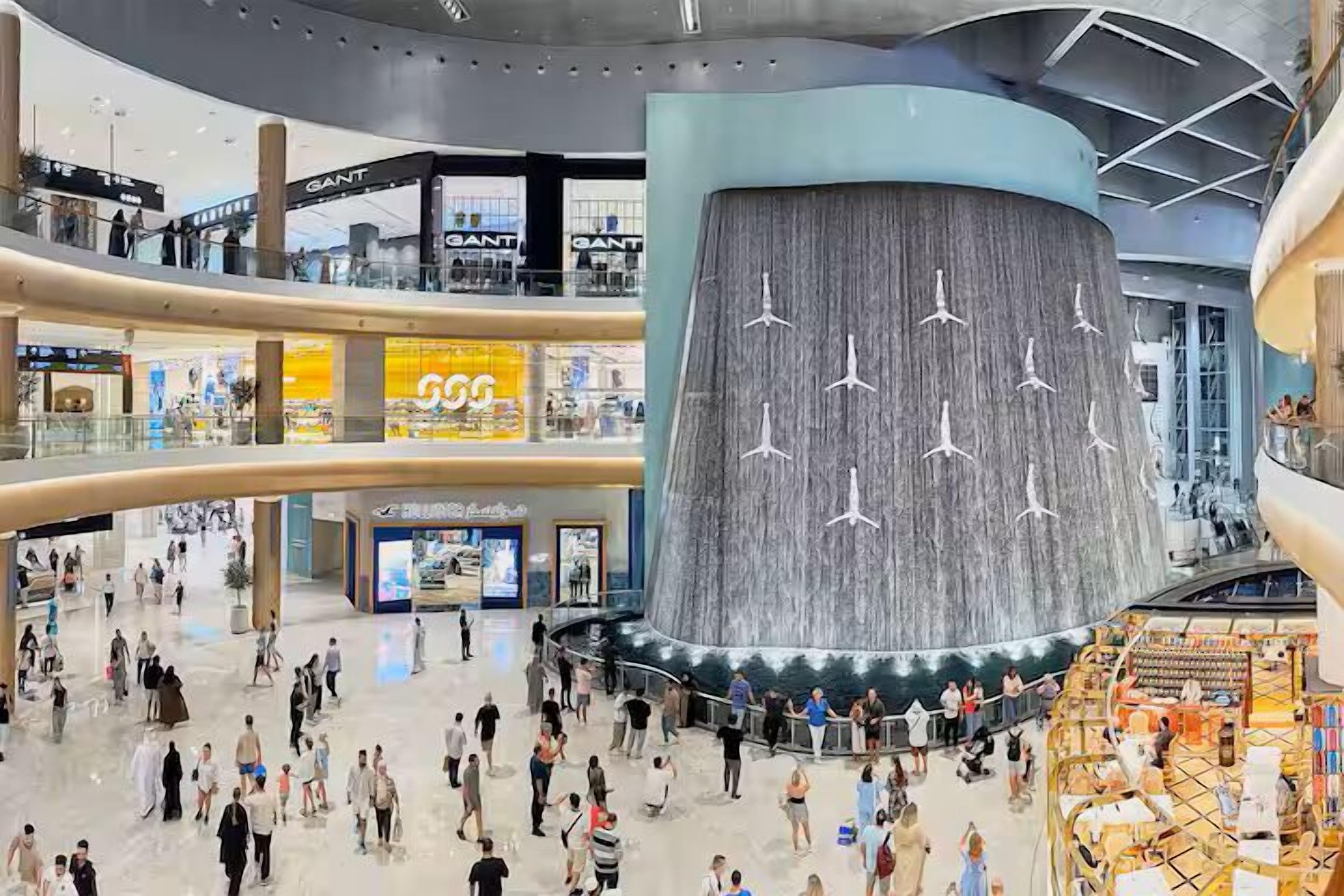 Un centro comercial de varios niveles con un atrio central que presenta una pared curva grande con lámparas colgantes.
