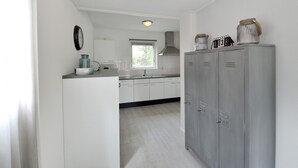 A kitchen with white cabinets, a window, a sink, and a clock on the wall. - Summio Villapark Schildmeer (Steendam)