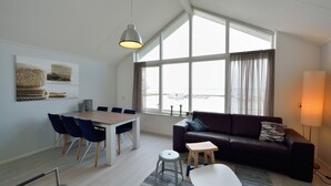 A modern living room with a large window, a dining area, and a sofa. - Summio Villapark Schildmeer (Steendam)