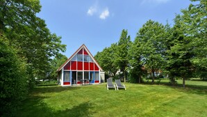 A red and white house with a triangular roof, surrounded by lush green trees and a well-maintained lawn. - Summio Villapark Schildmeer (Steendam)