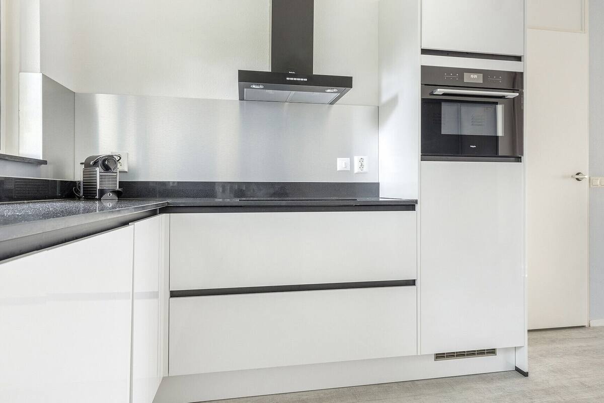 A modern kitchen with white cabinets, a black countertop, a built-in oven, and a stainless steel range hood.