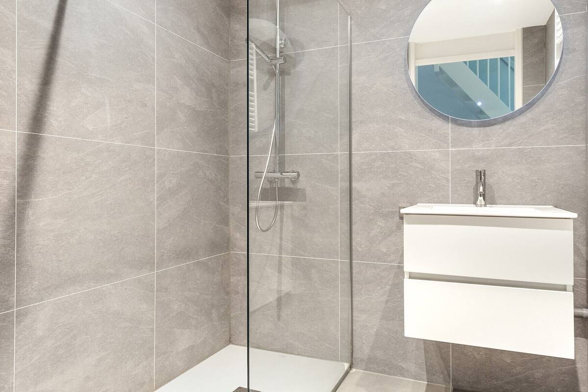 A modern bathroom with a glass-enclosed shower, a white vanity with a mirror, and a tiled floor.