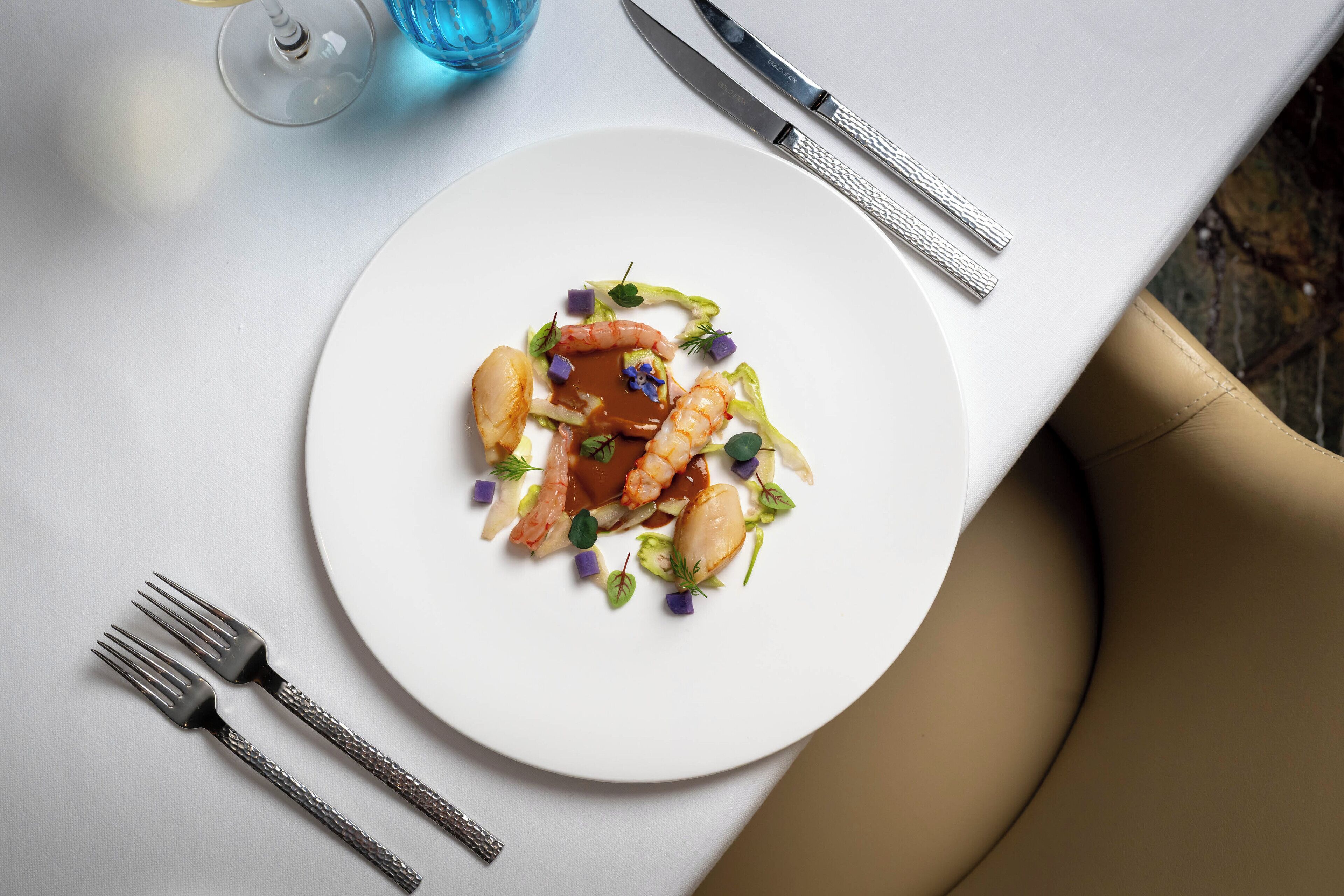 Un plato blanco con un plato de mariscos, acompañado por un tenedor y un cuchillo sobre una mesa.