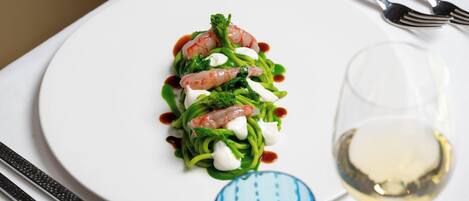 A white plate with a seafood dish, a blue glass, and a wine glass on a table.