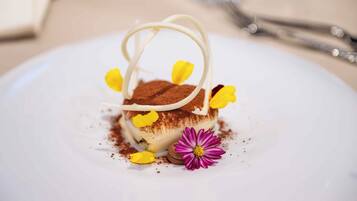 Un dessert su un piatto bianco, con un fiore viola e petali gialli.