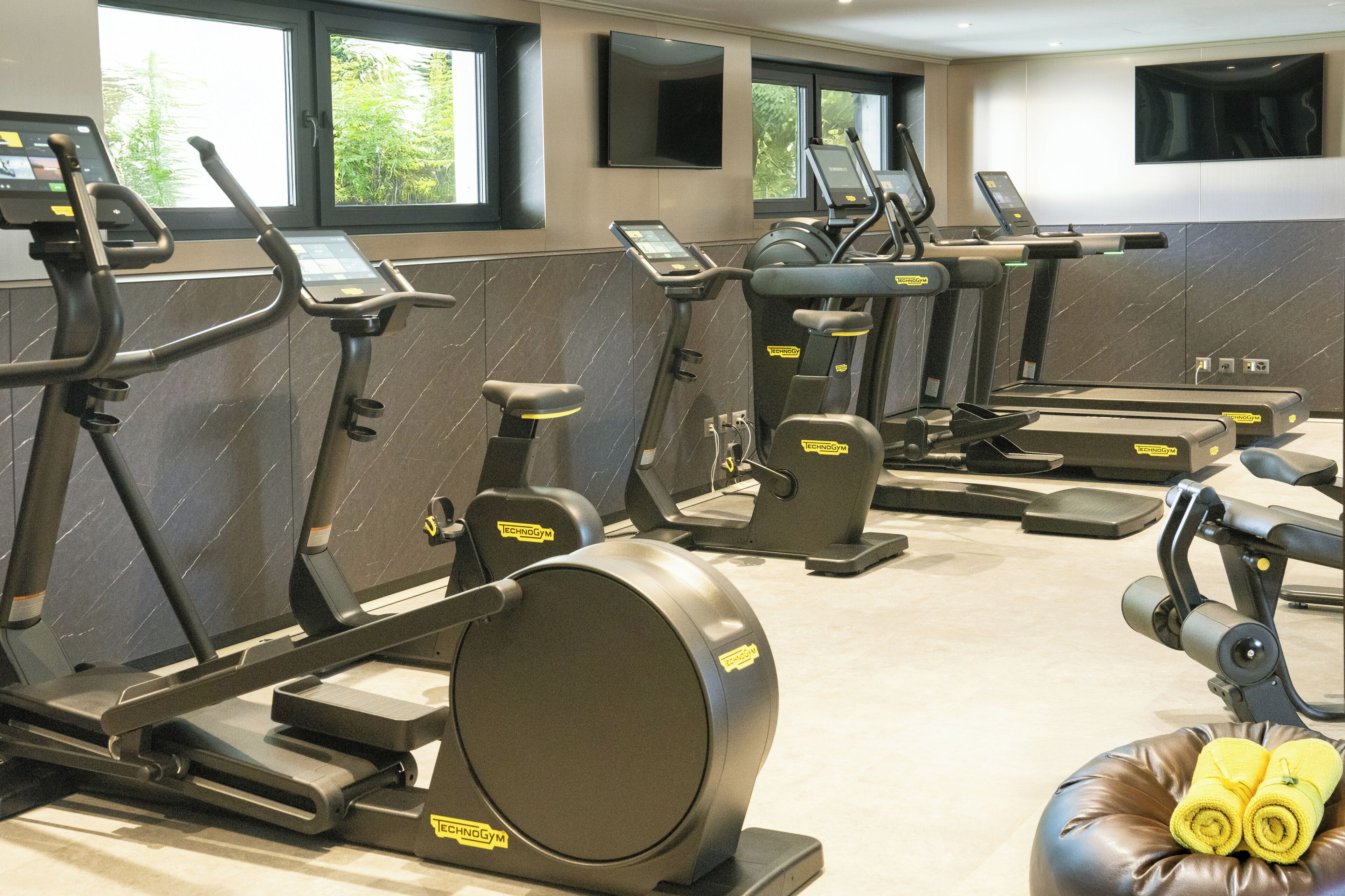 Une salle de sport équipée de plusieurs appareils d’exercice, d’un tapis de course et d’un banc avec des serviettes.