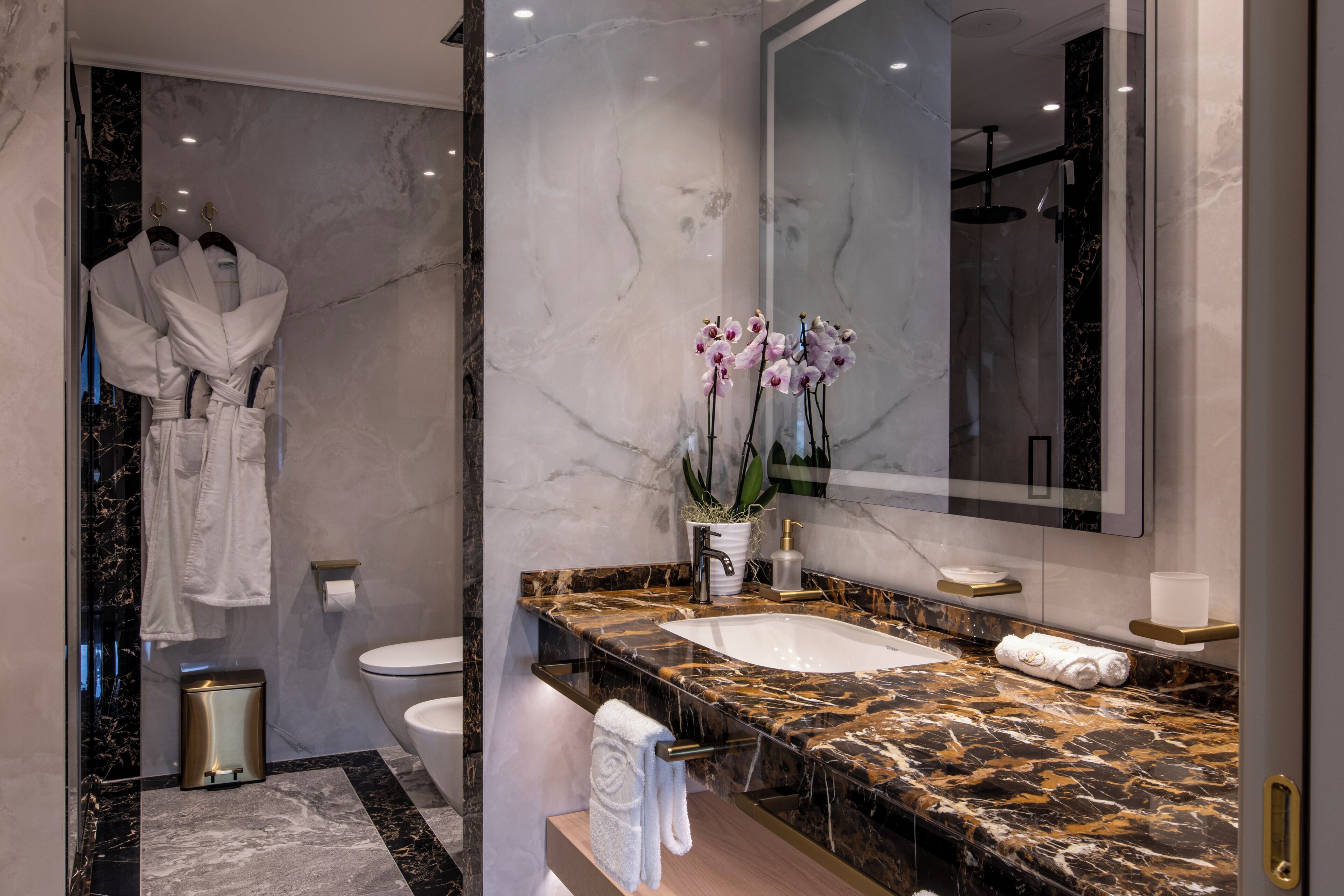 Un baño moderno con tocador de mármol, un espejo grande y cabina de ducha de vidrio.