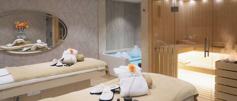 Une salle de spa équipée de deux tables de massage, d’un sauna et d’un grand miroir.