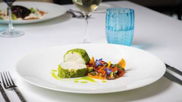 Un plato blanco con un guiso verde, una ensalada y una copa de vino blanco sobre una mesa.