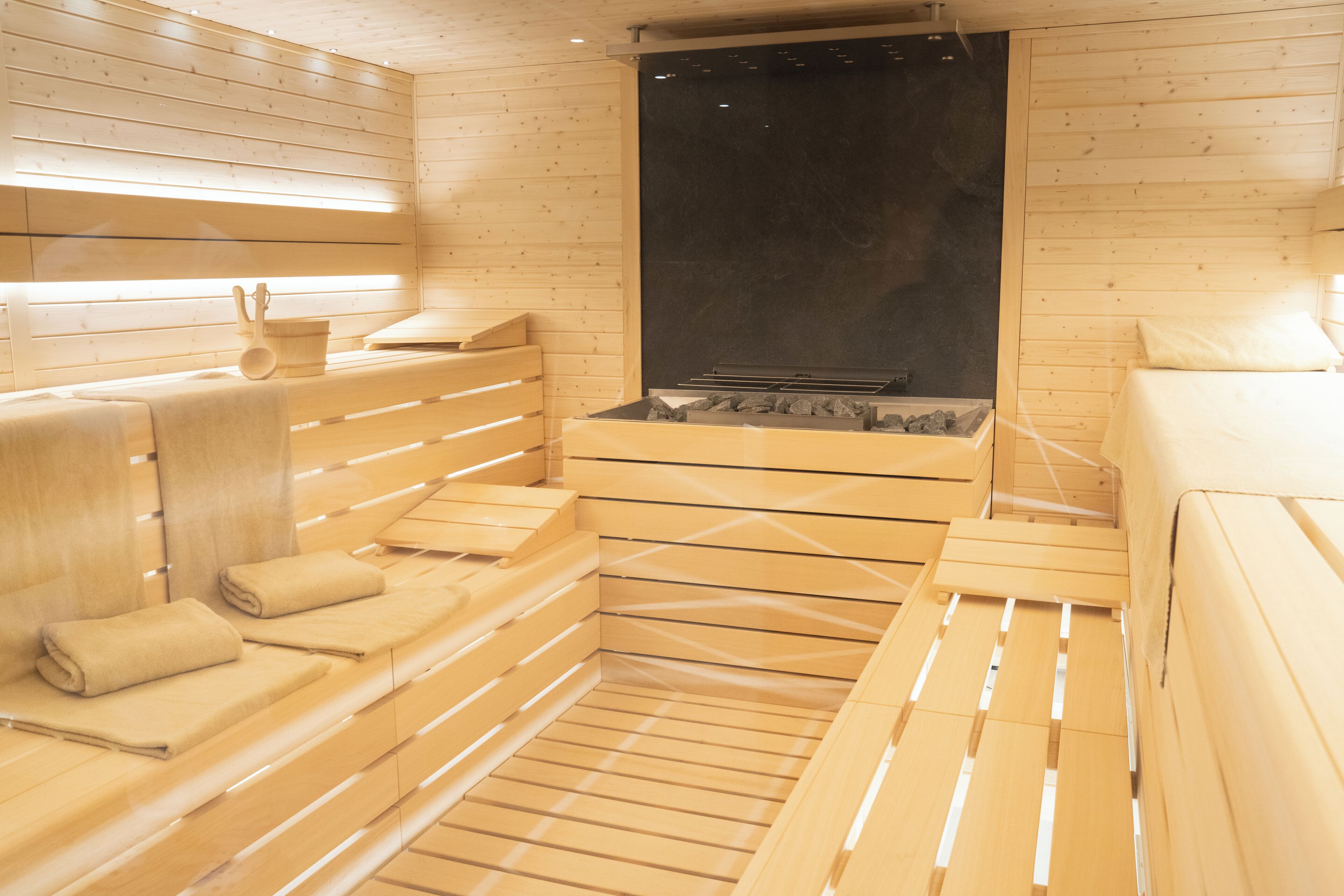 A sauna room with wooden benches and a black wall.