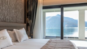 A hotel room with a large bed, a view of a lake and mountains, and a patterned wall. - Swiss Diamond Boutique Hotel La Romantica (Melide)