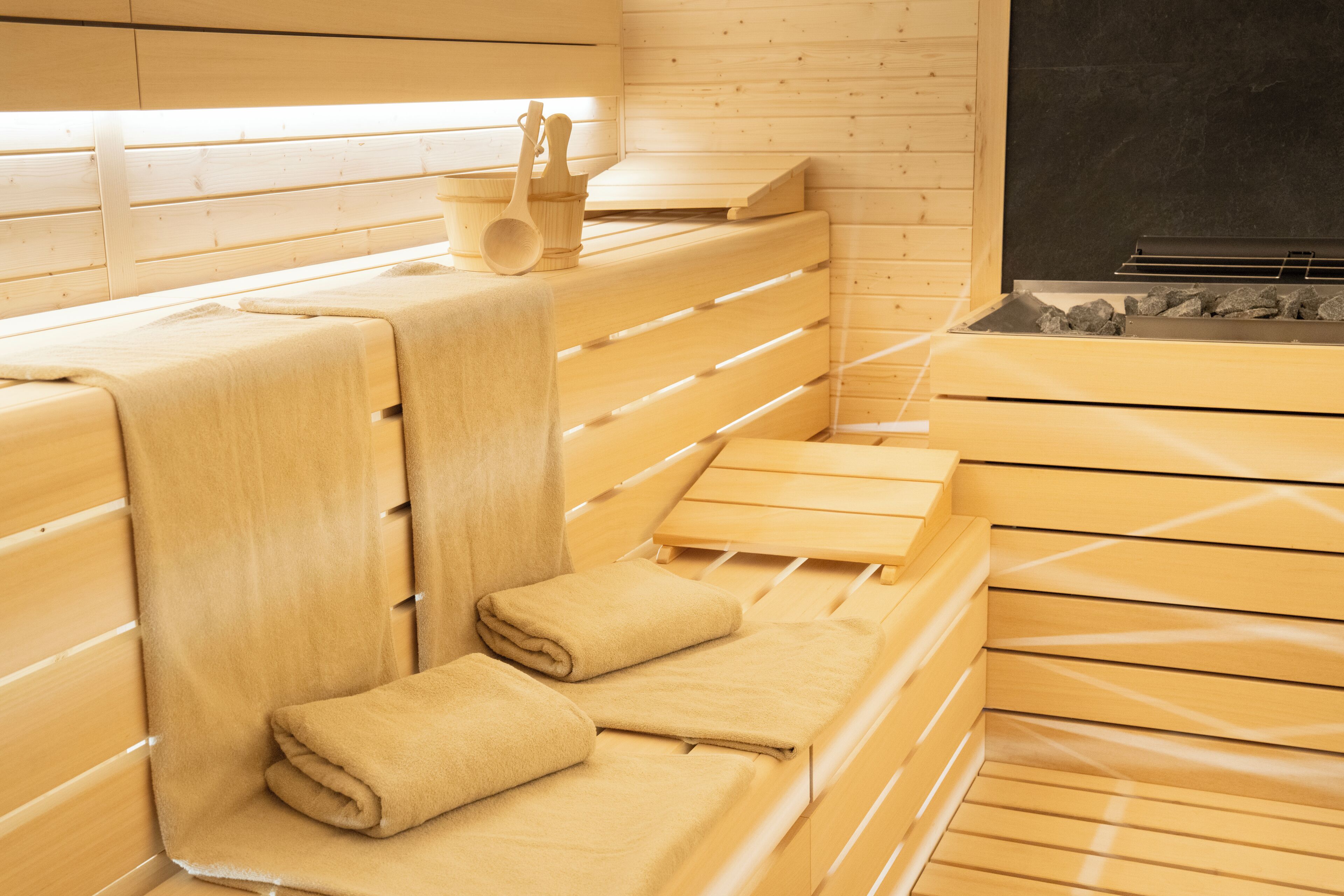 A sauna with wooden benches and benches, towels, and a stone basin.