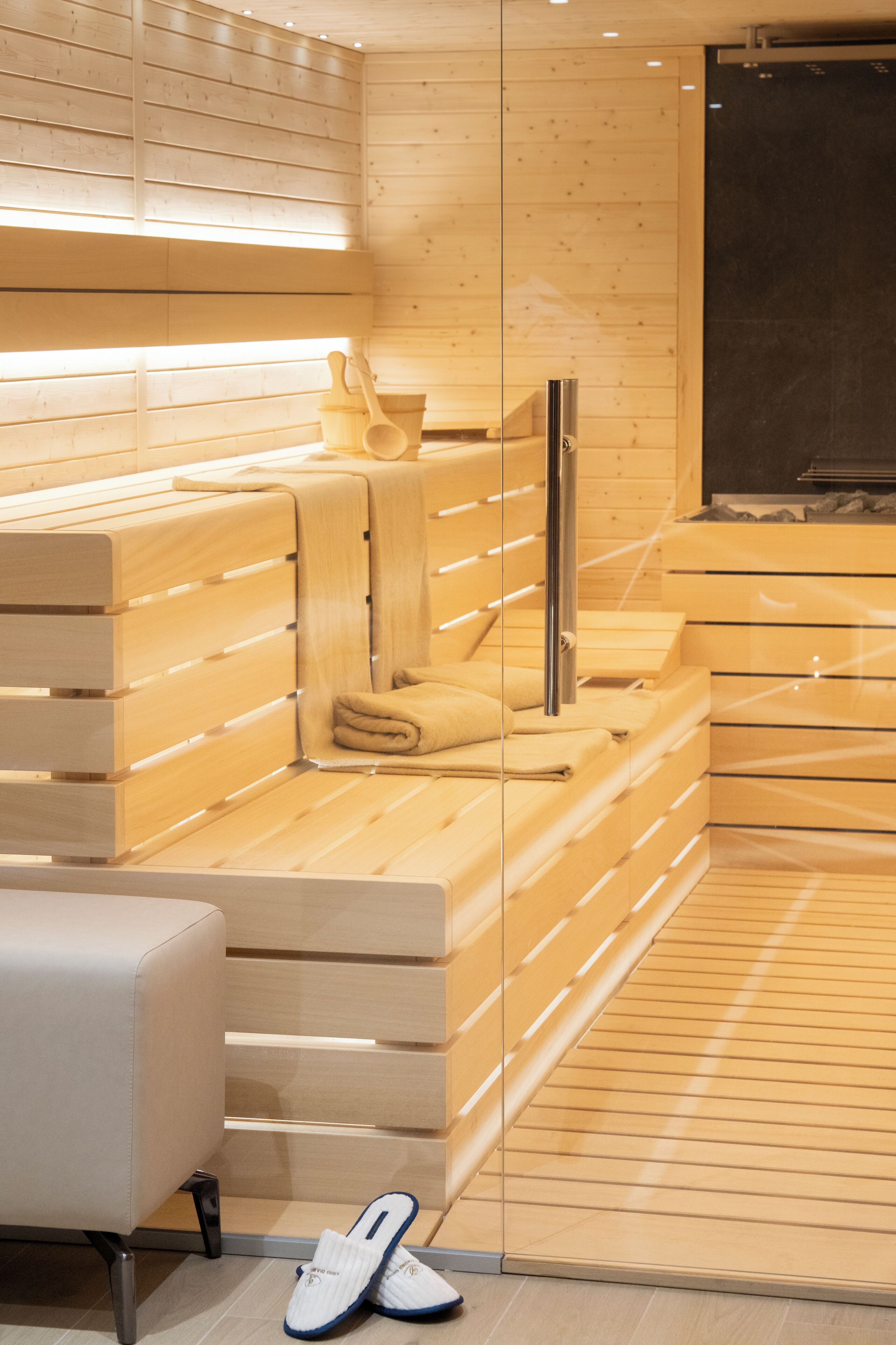 A modern sauna with wooden slats, a glass partition, and a bench.