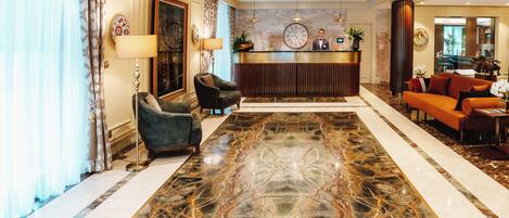 Un vestíbulo de hotel con piso de mármol, una recepción y zonas de estar.