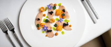 A white plate with a seafood dish, accompanied by a fork and knife on a table.