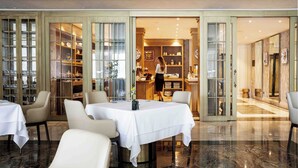 A restaurant with a marble floor, white tablecloths, and a person in the kitchen. - Swiss Diamond Boutique Hotel La Romantica (Melide)