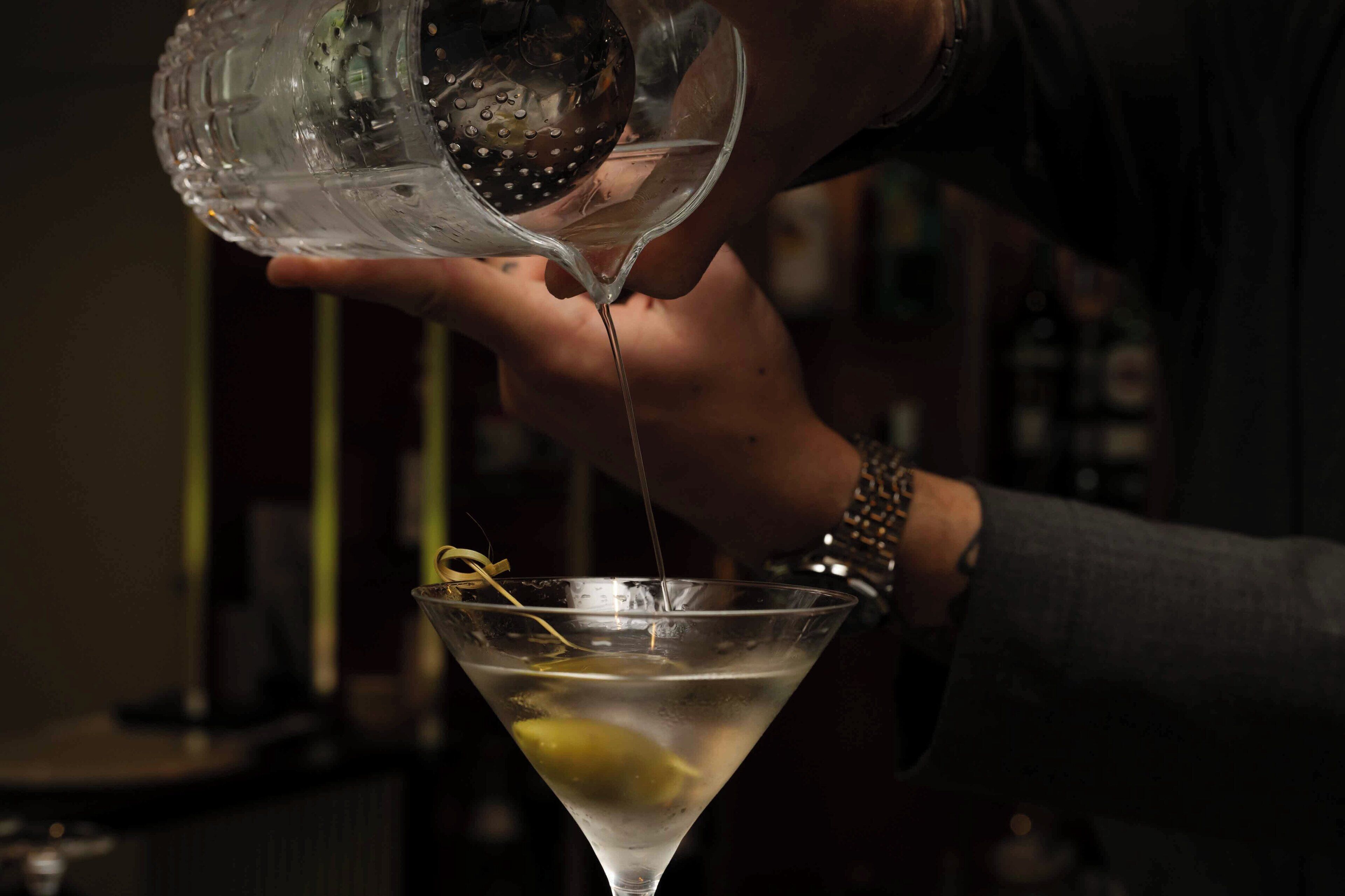 A person pouring a clear liquid into a martini glass with a lemon slice.